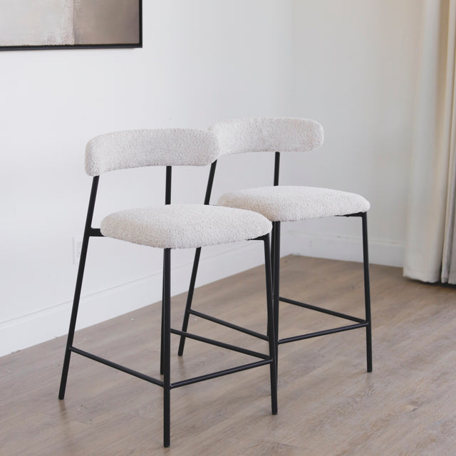 Paire de tabourets en tissu crème bouclé avec pieds metalliques noirs.