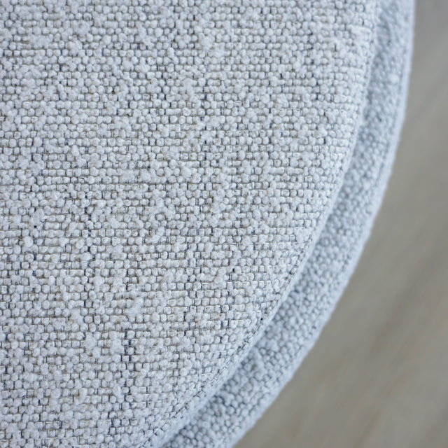 Image rapprochée d'un Pouf rond en tissu bouclé gris avec plateau noir amovible sur sol en bois clair.