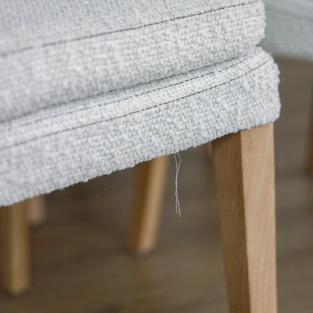 image rapprochée d'un ensemble de chaises modernes en tissu bouclé ivoire avec pieds en bois pâle avec défaut d'un fil tiré.
