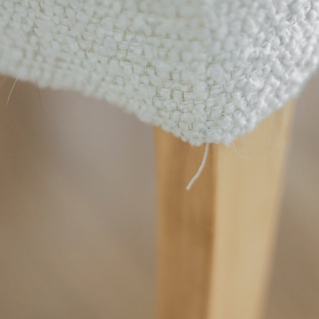 image rapprochée d'un ensemble de chaises modernes en tissu bouclé ivoire avec pieds en bois pâle avec défaut d'un fil tiré.