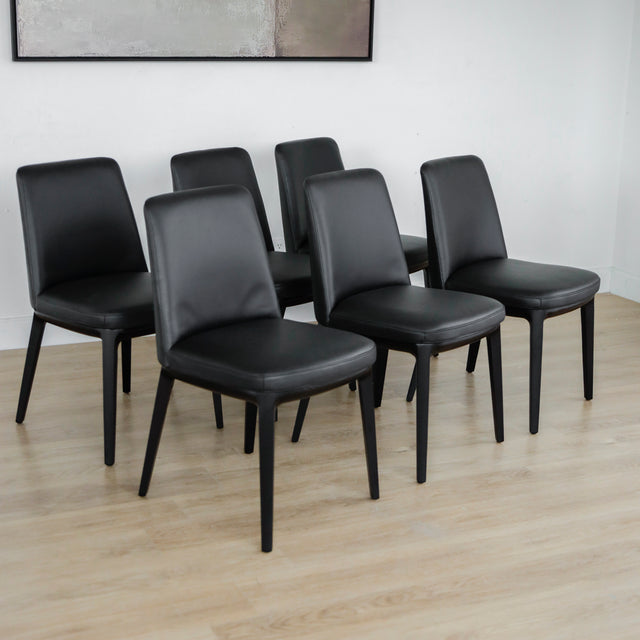 ensemble de six chaises modernes en cuir noir avec pieds en bois noir sur parquet clair.