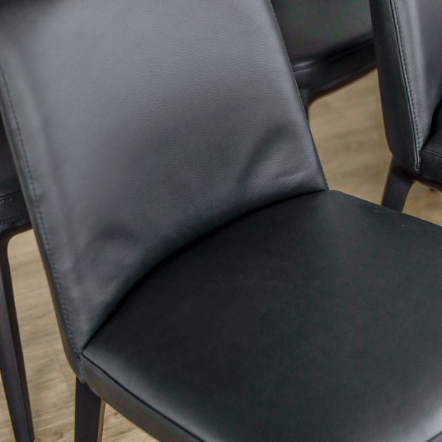 image rapprochée d'un ensemble de six chaises modernes en cuir noir avec pieds en bois noir sur parquet clair.