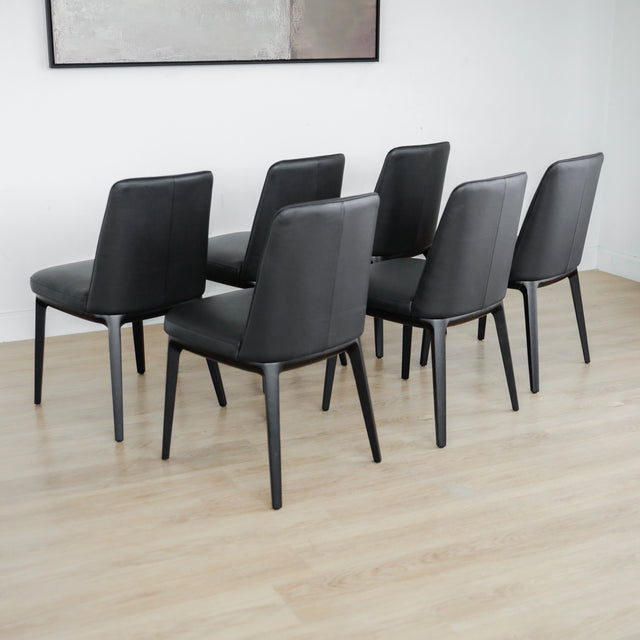 ensemble de six chaises modernes en cuir noir avec pieds en bois noir sur parquet clair.