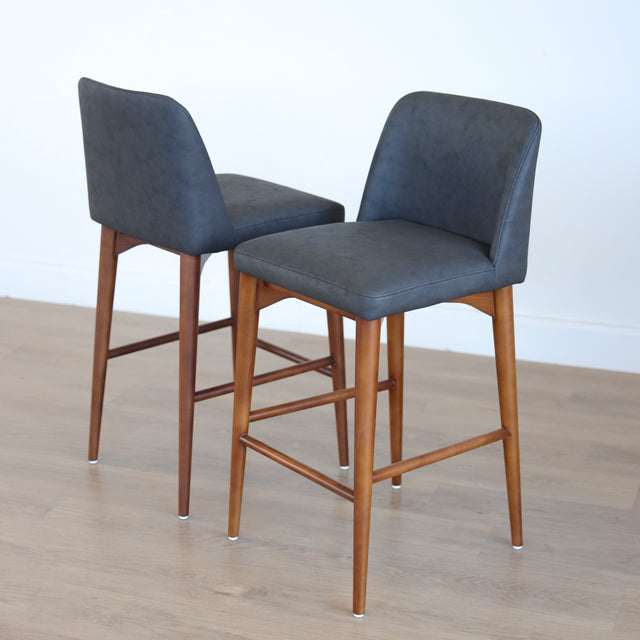 Deux tabourets de comptoir en cuir végane noir avec pieds en bois noyer, style moderne pour cuisine ou salon.