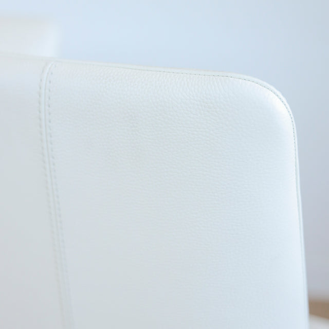 Image rapprochée d'une chaise moderne en cuir blanc avec pieds en bois couleur noyer, design pure pour salle a manger contemporaine.