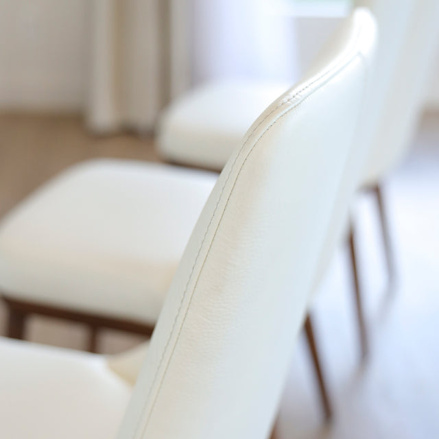 Image rapprochée d'une chaise moderne en cuir blanc avec pieds en bois couleur noyer, design pure pour salle a manger contemporaine.