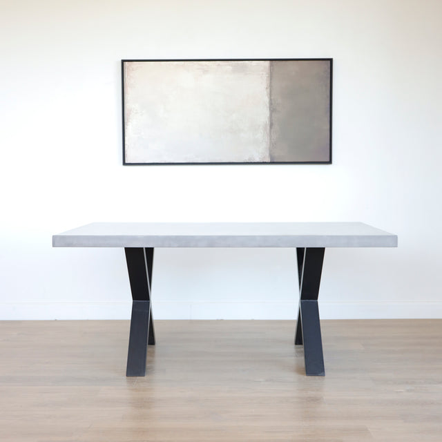 Table rectangulaire en beton avec pieds en metal noir en X, style industriel moderne.