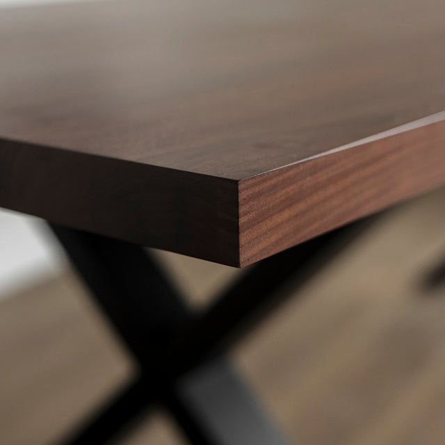 Image rapprochée d'une table rectangulaire en bois fonce avec pieds en metal noir en X, style industriel contemporain.