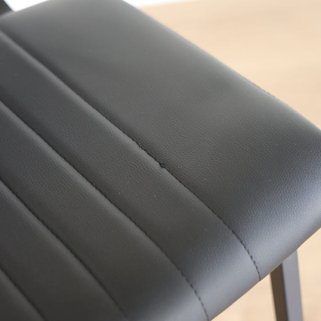 Image rapprochée de Quatre chaises noires en simili cuir avec pieds en metal, design moderne pour salle a manger.