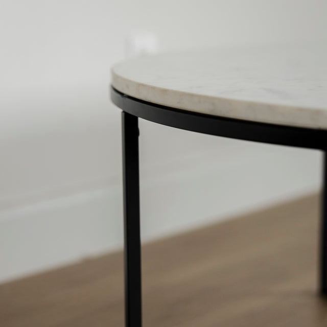 Image rapprochée d'une Table basse ronde avec plateau en marbre blanc et structure en metal noir, style moderne et minimaliste.