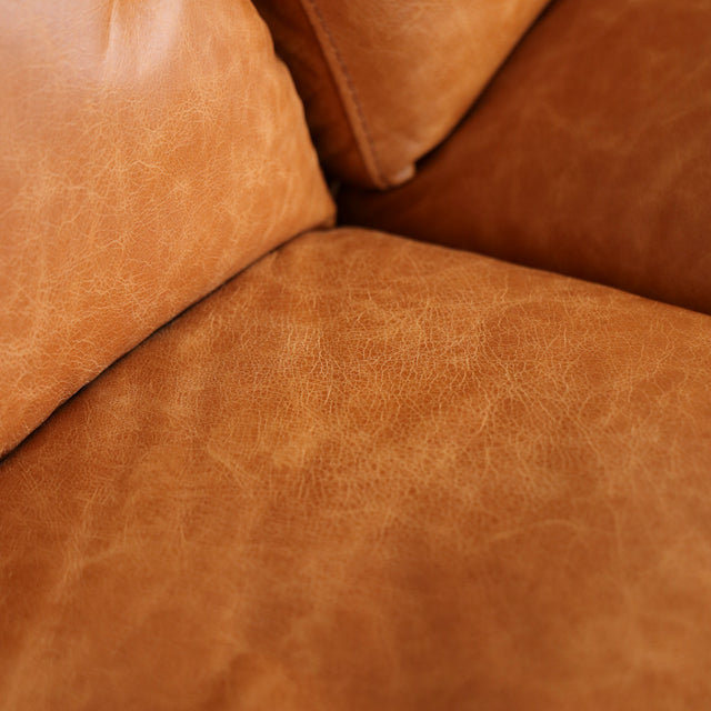 Image rapprochée d'un canape inclinable en cuir brandy au design contemporain avec accoudoirs larges et assises confortables.