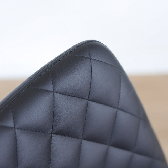 Chaise noire matelassee a dossier capitonne et pieds metal fins.