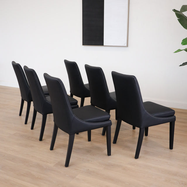 Lot de 4 chaises de cuisine, cuir végane noir, pattes noires, avec coutures contrastantes dans un décor moderne et lumineux.