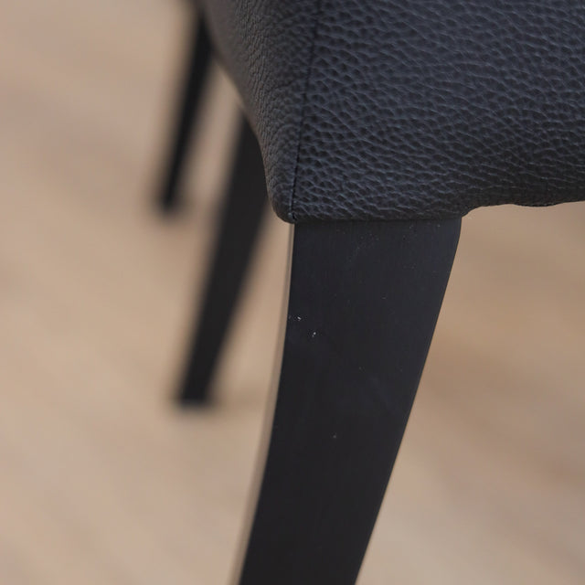 Lot de 4 chaises de cuisine, cuir végane noir, pattes noires, avec coutures contrastantes dans un décor moderne et lumineux.