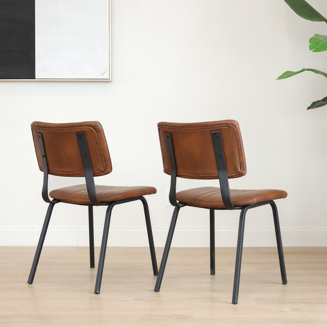 Deux chaises de salle à manger en cuir végane cognac, piètement métal noir, style industriel moderne.