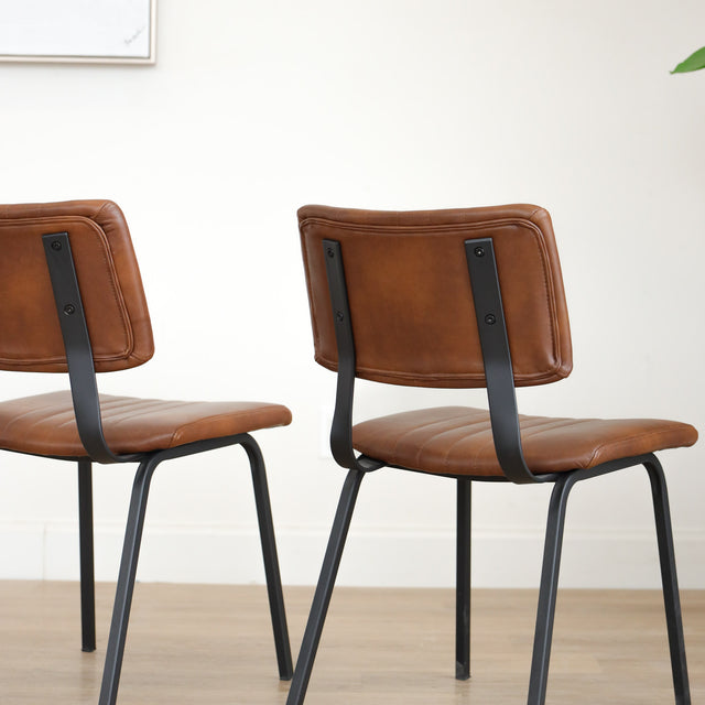 Deux chaises de salle à manger en cuir végane cognac, piètement métal noir, style industriel moderne.