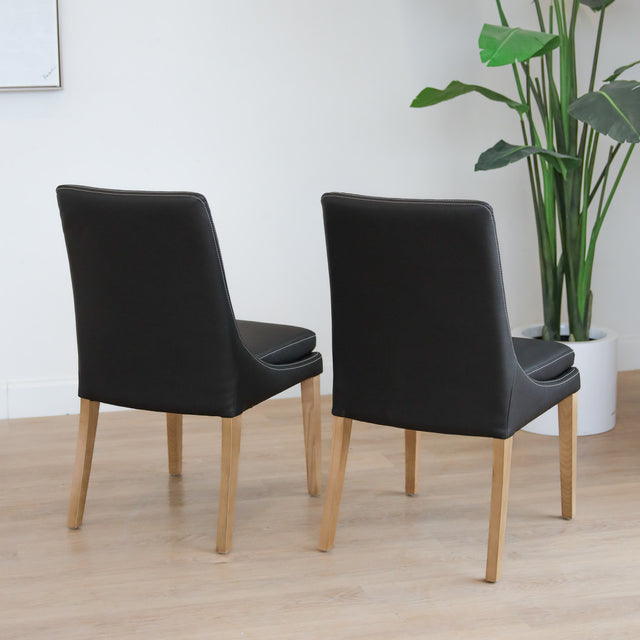 Lot de deux chaises de salle à manger en cuir végane noir avec pattes en bois pâle, design moderne et élégant.