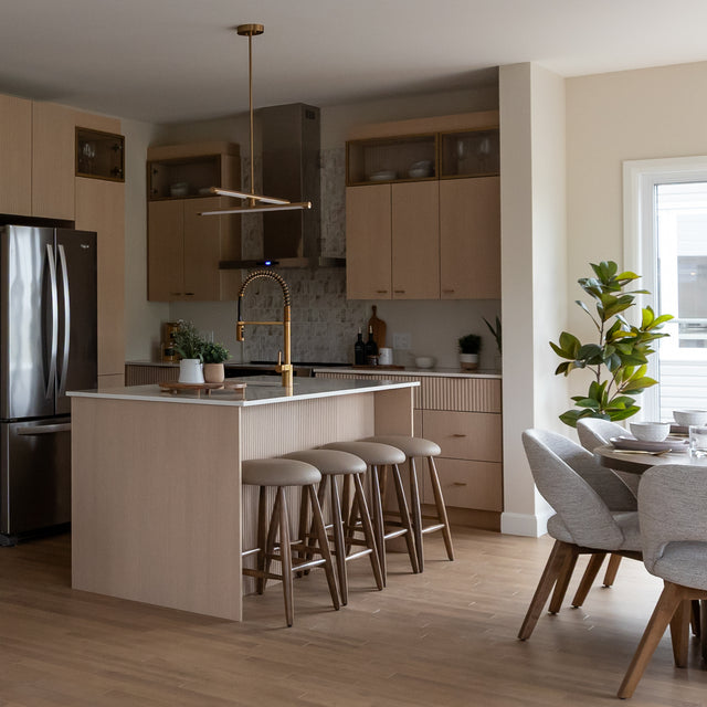 Quatre tabourets de bar en cuir végane taupe avec pieds en bois devant un ilot de cuisine moderne.