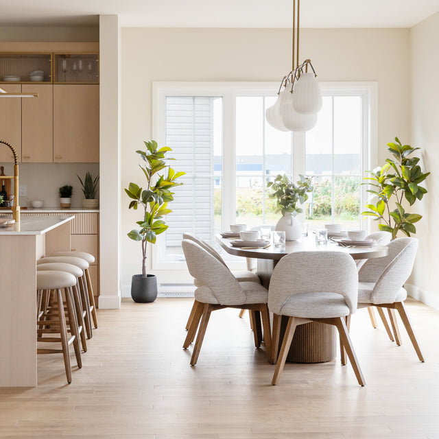 Salle a manger moderne avec table ronde en bois, chaises beige et ilot de cuisine assorti.