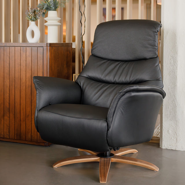 Fauteuil en cuir noir avec appui-tête et base bois pivotante, dans un intérieur chaleureux.