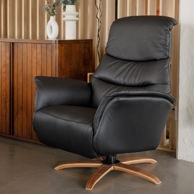 Fauteuil en cuir noir avec appui-tête et base bois pivotante, dans un intérieur chaleureux.