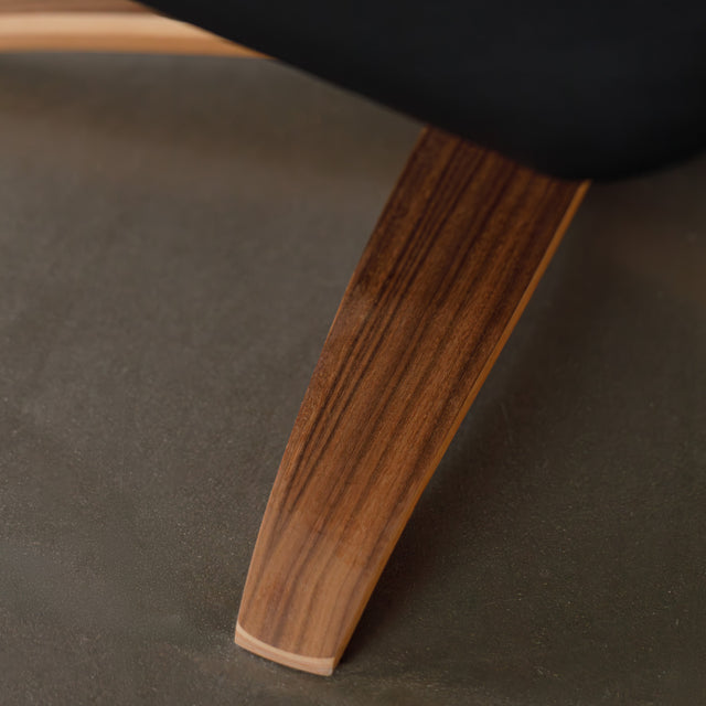 Fauteuil en cuir noir avec appui-tête et base bois pivotante, dans un intérieur chaleureux.