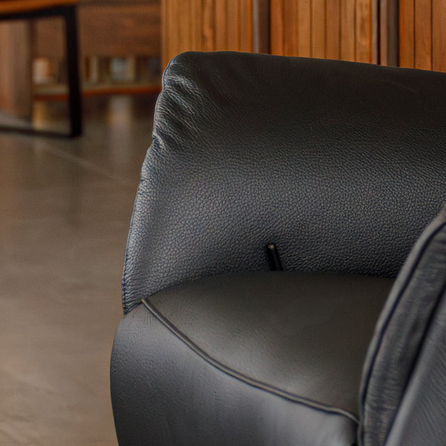 Fauteuil en cuir noir avec appui-tête et base bois pivotante, dans un intérieur chaleureux.
