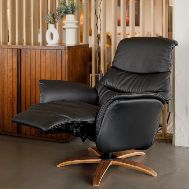 Fauteuil en cuir noir avec appui-tête et base bois pivotante, dans un intérieur chaleureux.