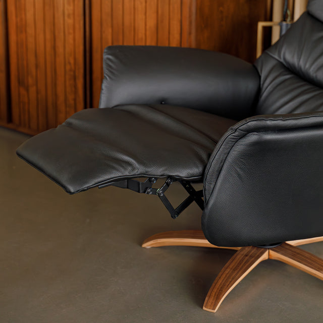 Fauteuil en cuir noir avec appui-tête et base bois pivotante, dans un intérieur chaleureux.