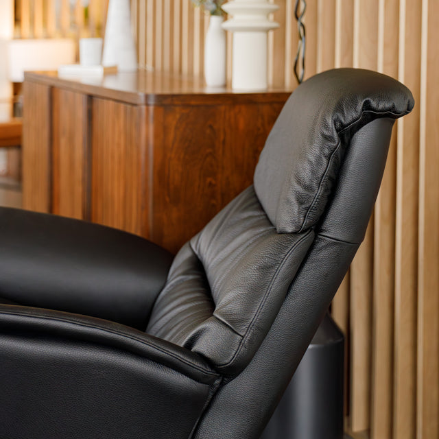 Fauteuil en cuir noir avec appui-tête et base bois pivotante, dans un intérieur chaleureux.