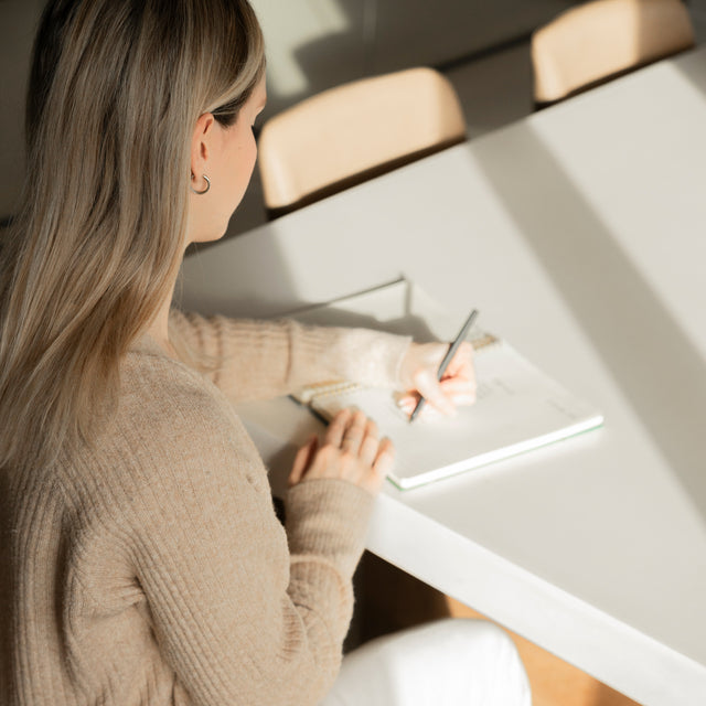 table en beton clair avec chaise en bois et personne ecrivant dans un carnet.