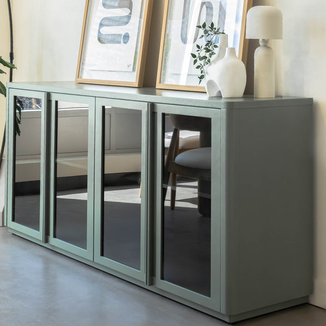 Buffet moderne vert sauge à portes vitrées fumées, décoré d’objets design dans un intérieur contemporain lumineux.