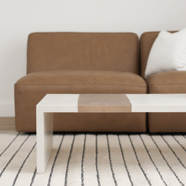 Table basse blanche avec bande centrale en bois clair devant canape brun.