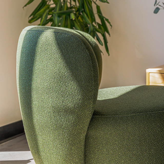 Fauteuil lounge vert en tissu bouclé avec base pivotante noire dans un salon moderne.