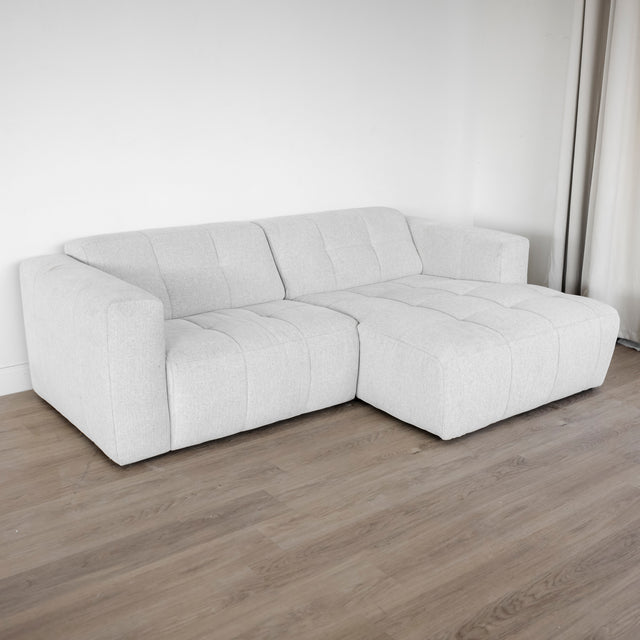 Canapé d’angle beige clair matelassé au style moderne et minimaliste.