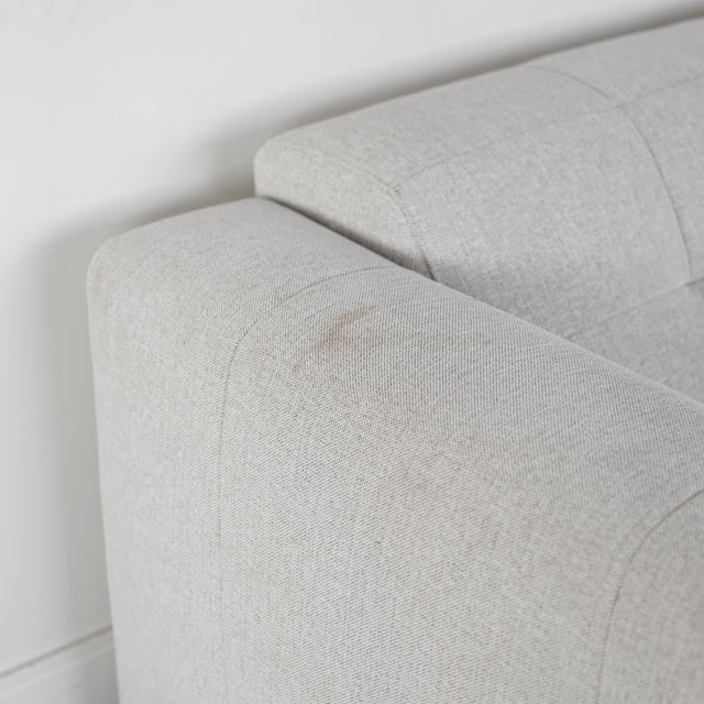 Détail de l’accoudoir du canapé beige clair en tissu texturé, avec une légère marque sur le revêtement.