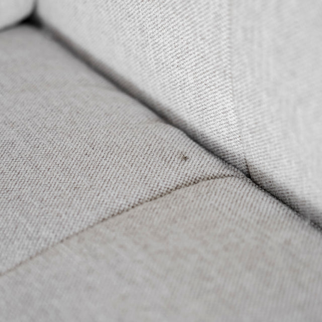 Gros plan sur la couture et la texture du tissu beige clair du canapé, mettant en valeur les détails du matelassage.