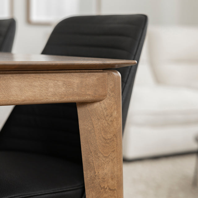 Detail du coin de table en bois naturel avec chaise noire et canape clair en arriere-plan.