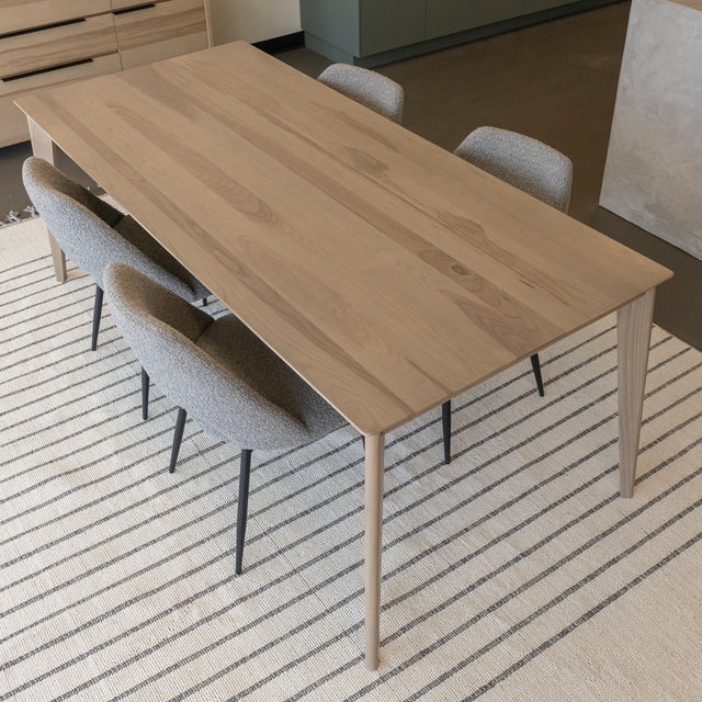 Table a manger en bois clair avec chaises grises sur tapis raye dans espace moderne.