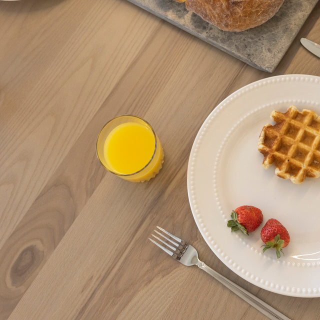 Petit dejeuner sur table en bois clair avec gaufre, fraises et verre de jus d’orange.