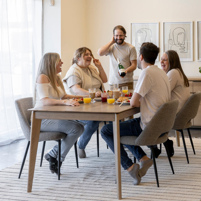 Table en bois clair avec chaises grises autour d’un repas convivial dans interieur moderne.