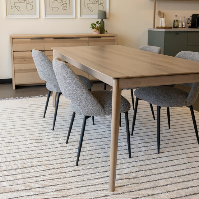 Table a manger en bois clair avec chaises grises sur tapis raye dans espace moderne.