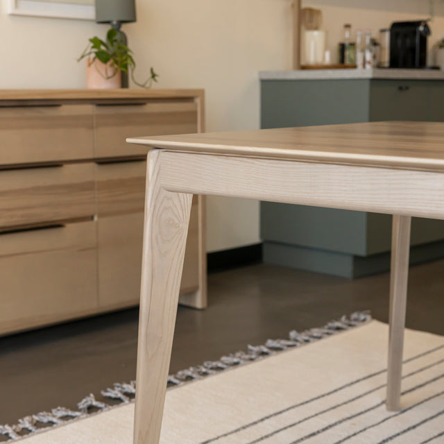 Coin de table en bois clair au design moderne sur tapis raye dans salle lumineuse.