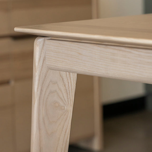 Coin de table en bois clair au design moderne sur tapis raye dans salle lumineuse.