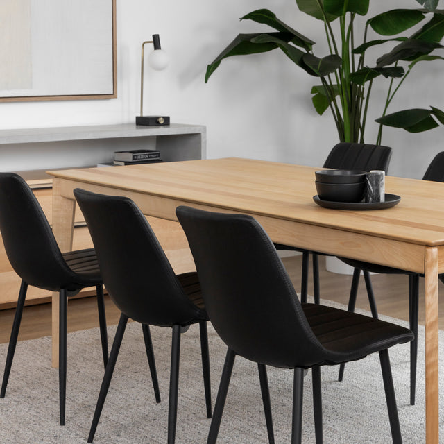 Table a manger en bois clair avec six chaises noires dans salle moderne et epuree.