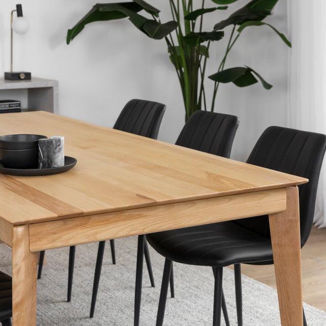Table a manger en bois clair avec chaises noires sur tapis beige dans salle lumineuse.