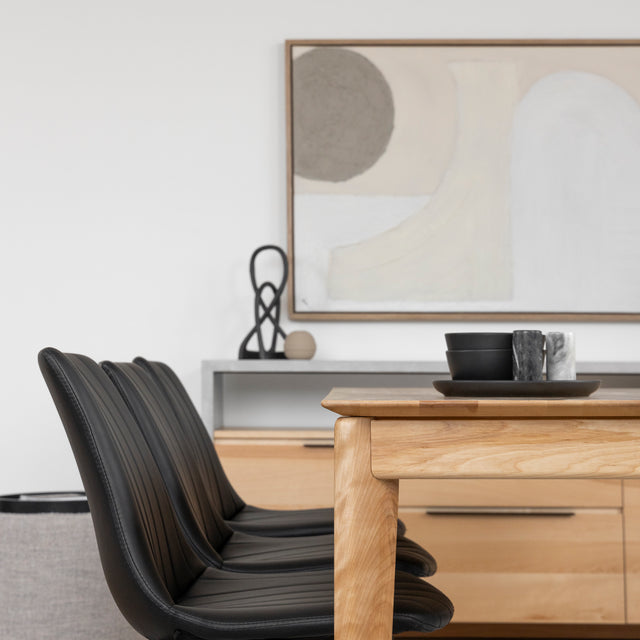Table en bois clair avec chaises noires et vaisselle moderne dans une salle a manger elegante.