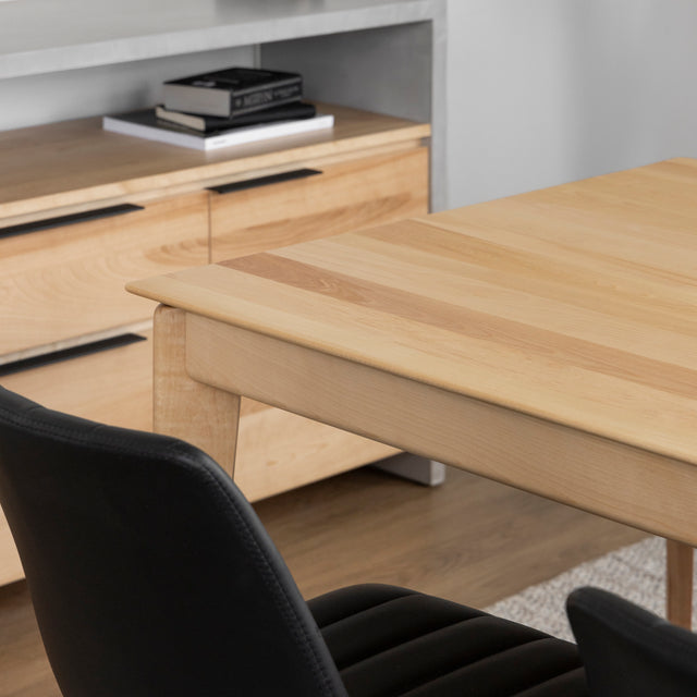 Coin de table en bois clair avec chaises noires et buffet assorti dans une salle moderne.