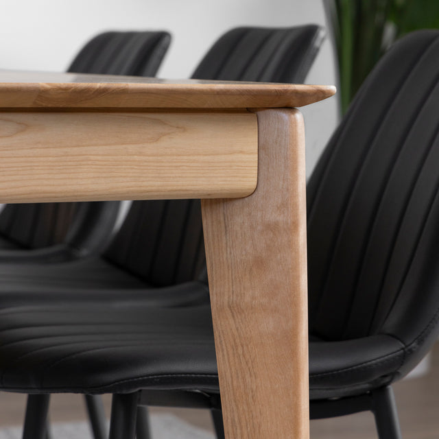 Table en bois clair avec chaises noires et vaisselle moderne dans une salle a manger elegante.