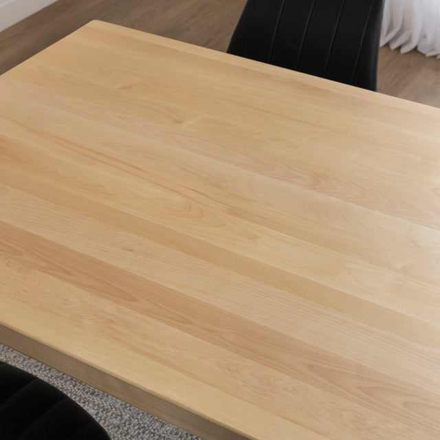 Surface de table en bois clair au fini lisse avec chaises noires et tapis beige.